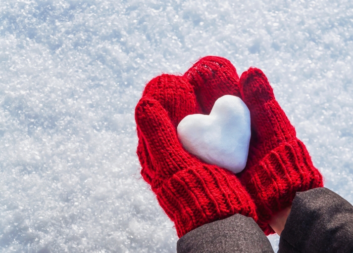 Female hands in knitted mittens with heart of snow in winter day